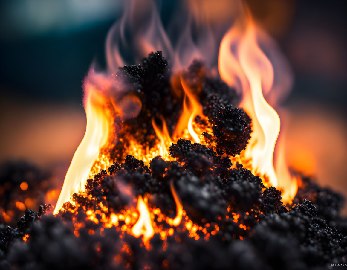 Intense flames consuming dark materials against a blurry blue and orange backdrop