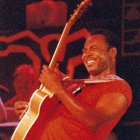 Smiling man with electric guitar on stage with band in warm lighting