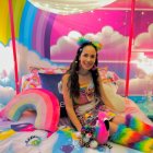 Colorfully dressed person on bed with whimsical decor and plush toys in vibrant room