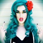 Vibrant turquoise curly hair woman with red flower accessory and pink lipstick gazes at camera