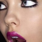 Detailed close-up: woman's face with orange eye makeup, dramatic eyelashes, glossy purple berry lips