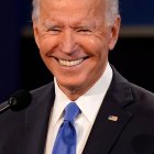 Smiling man with white hair in black suit and blue tie