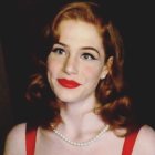 Portrait of woman with red hair, lipstick, and pearl necklace on dark background
