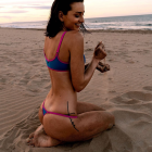 Woman in swimsuit holding shell on beach with splashing water and floating bubbles