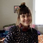 Smiling woman in black feathered outfit with floral accessories in a sunlit room