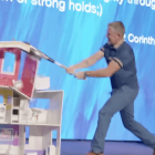 Female character cleaning dollhouse with broom, another watching, blue backdrop