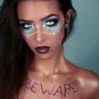 Blue-eyed woman with brown hair and glitter makeup on soft teal backdrop
