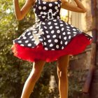 Woman in black and white polka-dot dress with red ruffles and accessories striking a playful pose