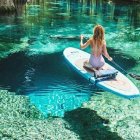 Red-haired person kneeling on paddleboard in serene forest waterway