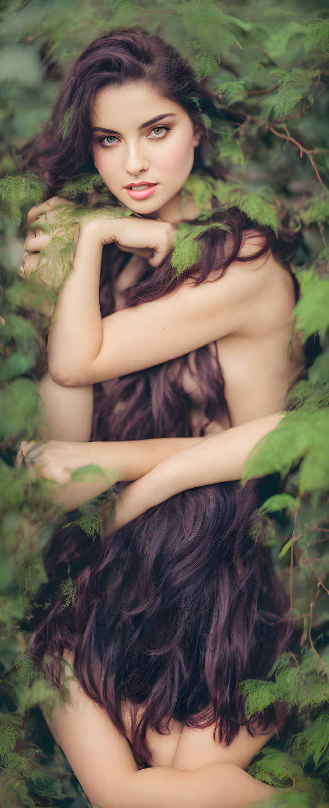 Woman with long dark hair in lush green foliage, gazing at the camera