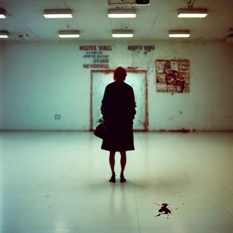 Red-haired person in dimly lit room with graffiti and dark spot