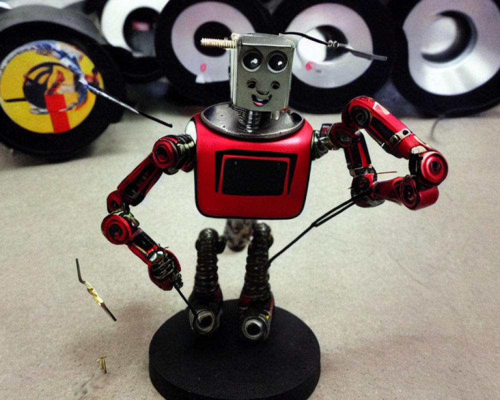 Red and Silver Robot Figurine with Square Head and Coiled Legs Standing by Disassembled Wheels