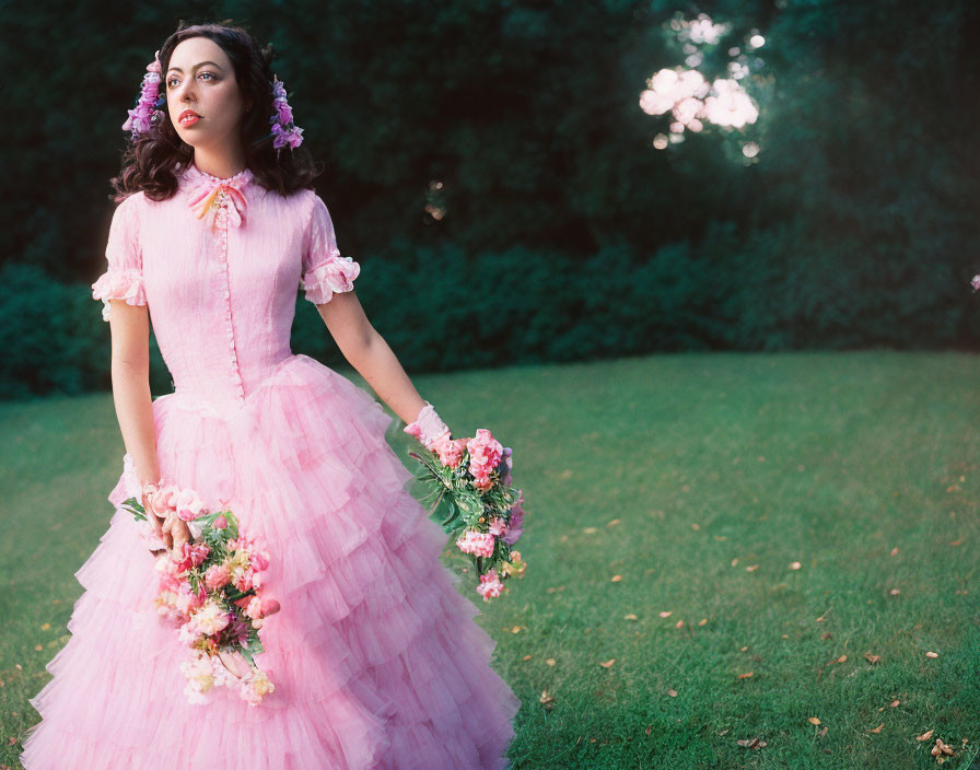 Woman in pink vintage dress with floral bouquet in lush green field