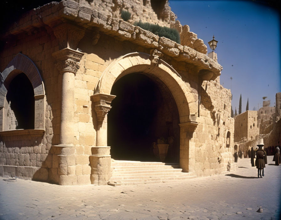 Stone archway, shadowy passage, people, historic buildings, clear blue sky