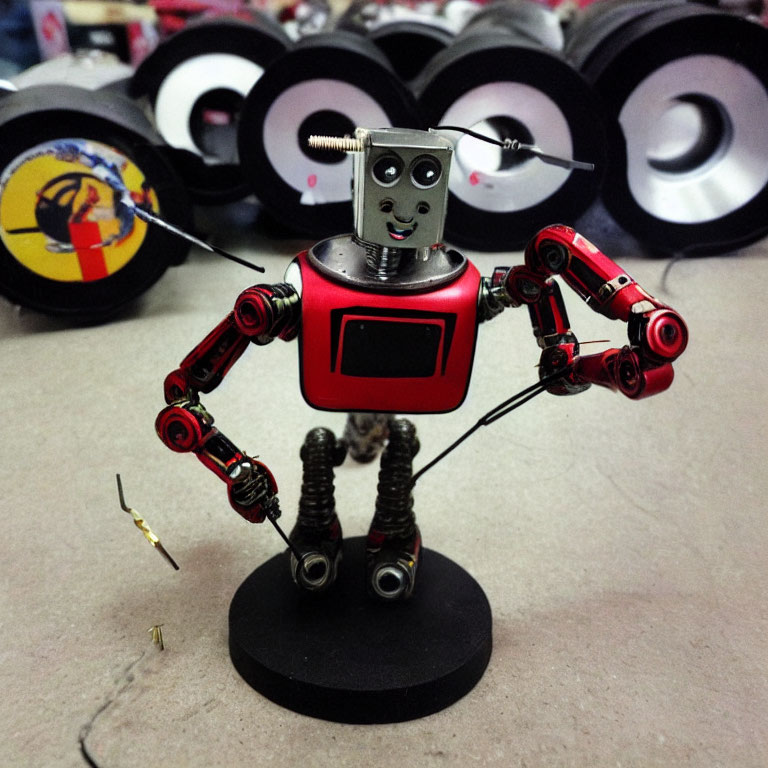 Red and Silver Robot Figurine with Square Head and Coiled Legs Standing by Disassembled Wheels