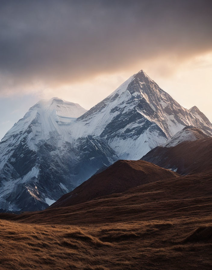 Snow-capped mountain peak above golden hills under dramatic sky