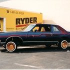 Classic Blue Car Painting Parked in Front of Yellow Buildings