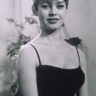 Young woman with yellow flower in hair, black dress, floral backdrop