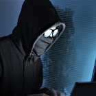 Hooded figure working on computer in dark room