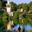 Scenic landscape with lake, traditional houses, lush flora, blue-and-white tower