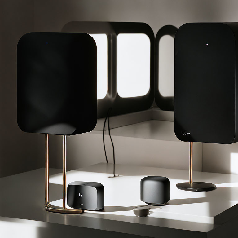 Black speakers with metal stands on white surface with shadow patterns