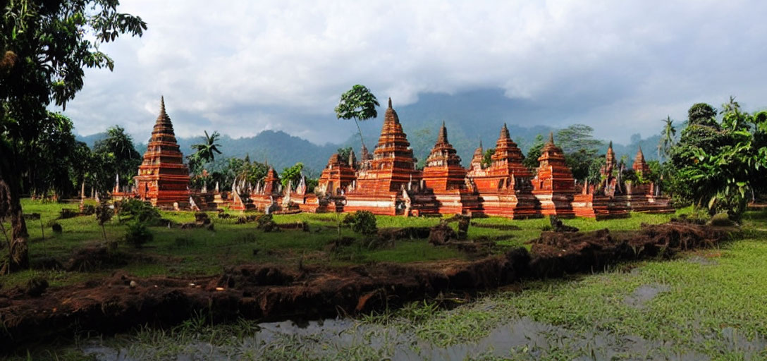 Ancient reddish-brown stupas in lush greenery with misty mountain backdrop.