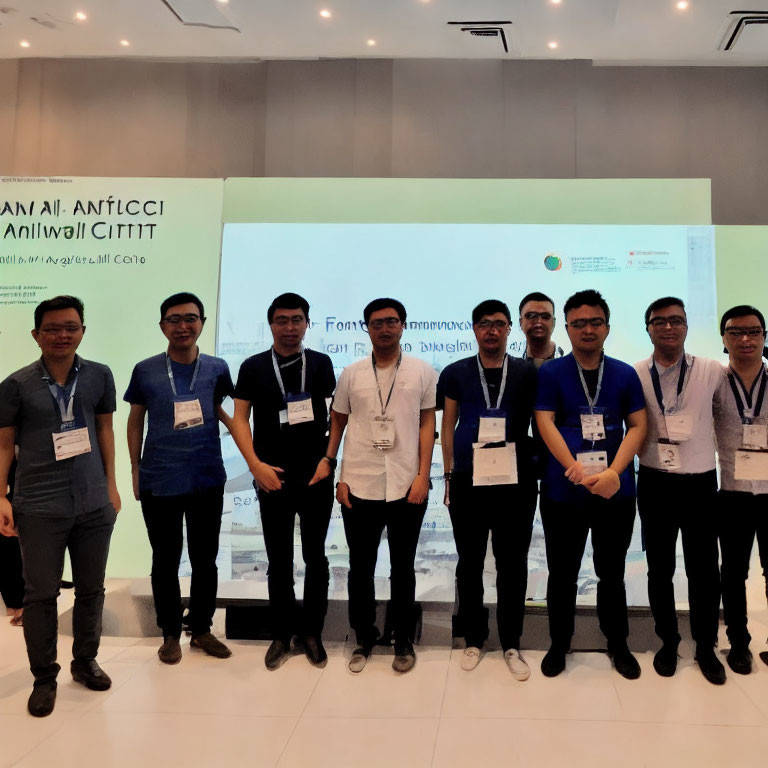 Nine Men in Professional Attire Smiling Before Conference Banner