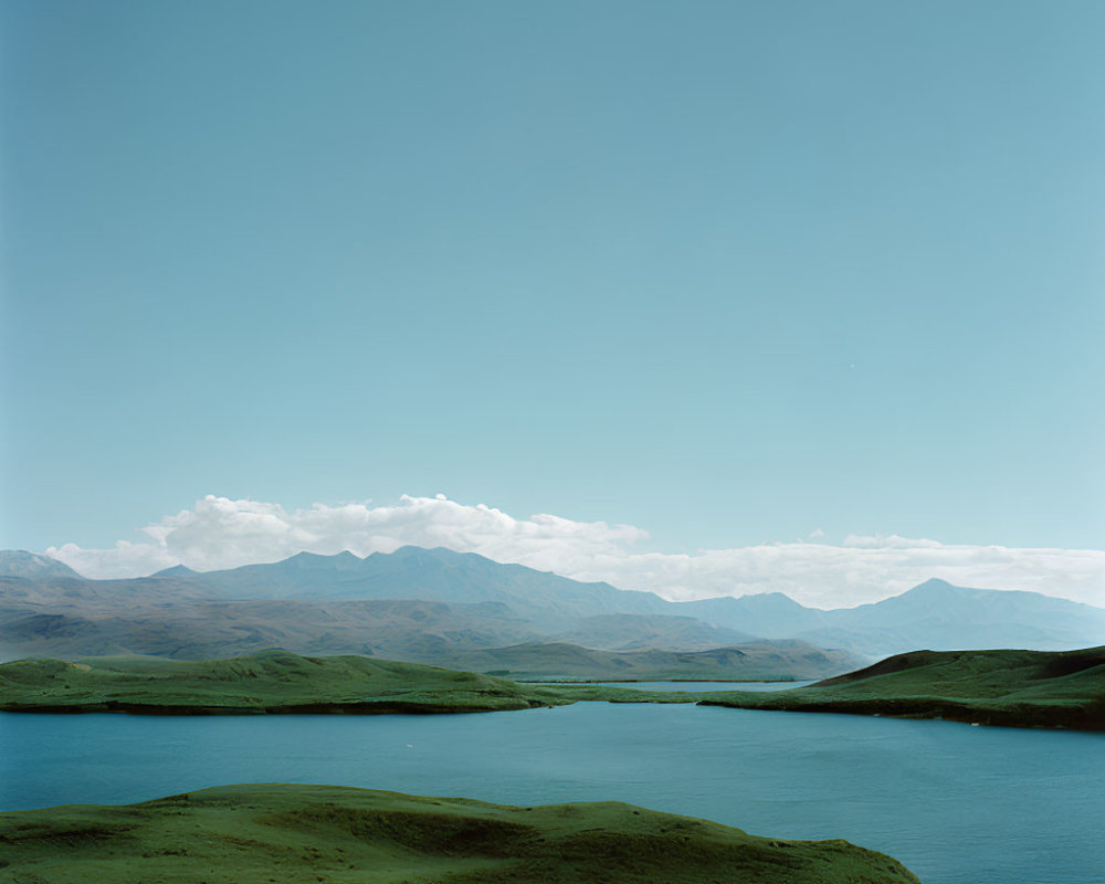 Tranquil landscape with green hills, blue lake, and mountains