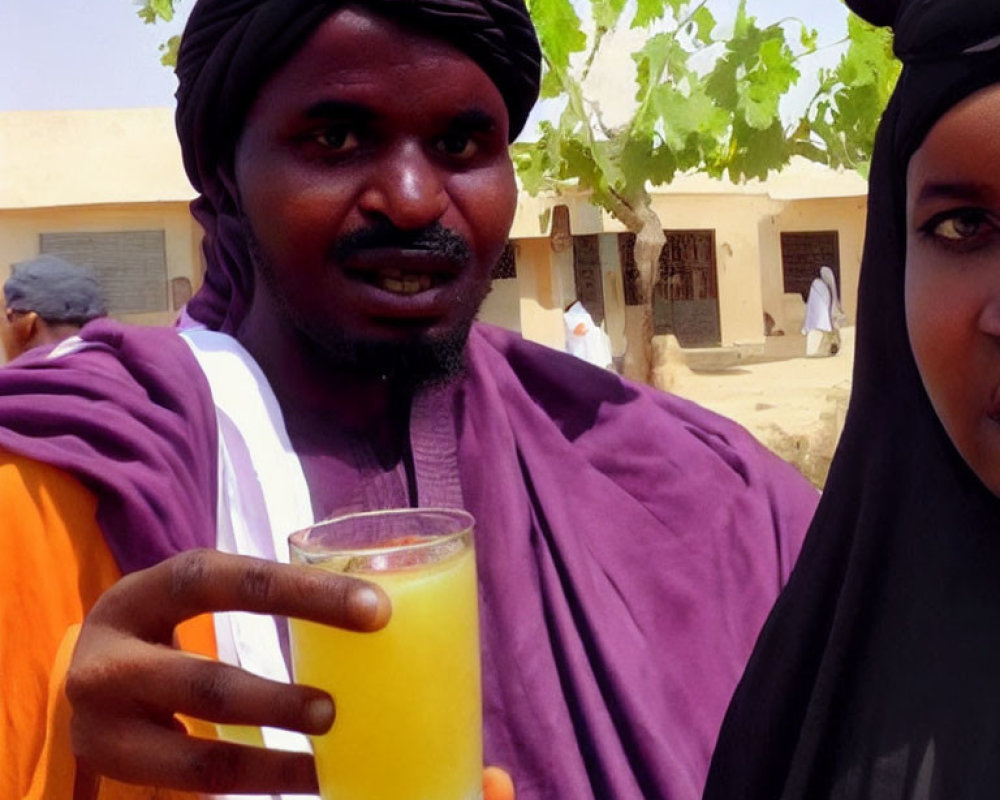 Man in traditional attire holds orange juice next to woman in hijab with buildings.