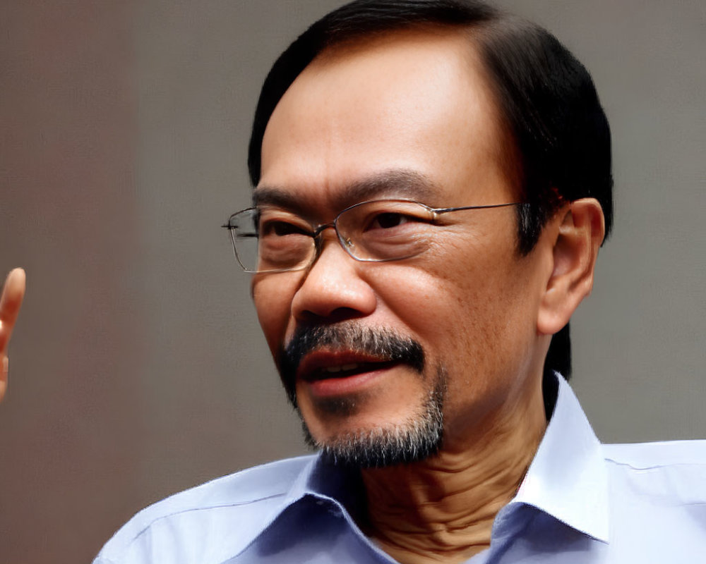 Middle-aged man with goatee and glasses in blue shirt smiling slightly