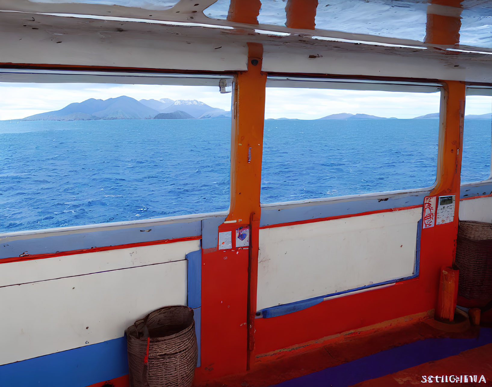 Serene blue sea and distant mountains through boat's colorful windows