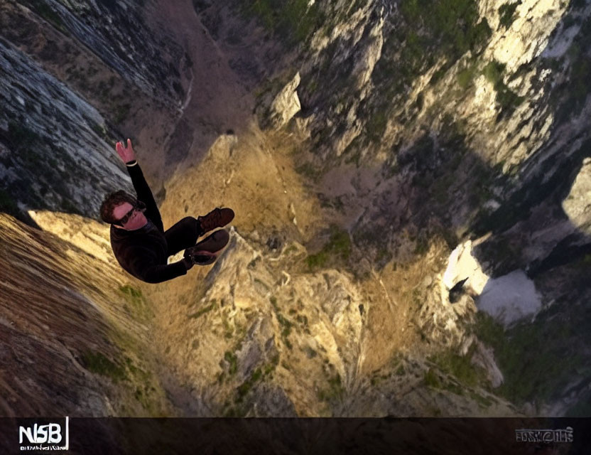 Person base jumping off cliff into deep rocky valley in free-fall position