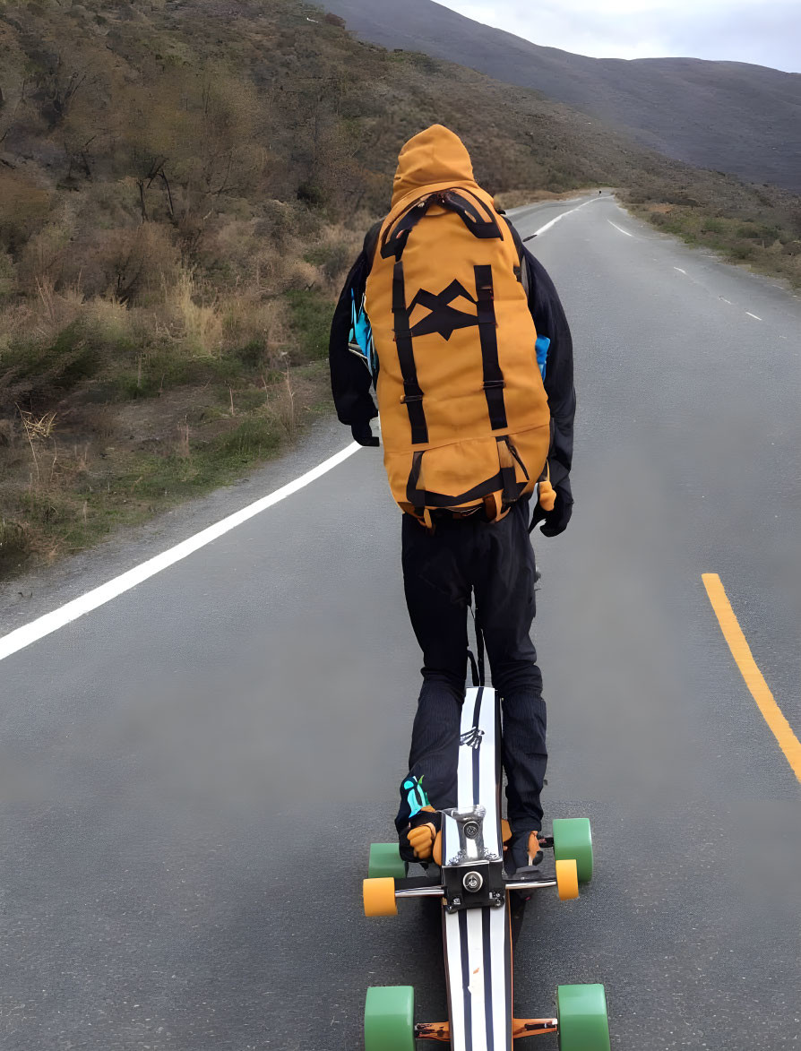 Person Longboarding Quiet Road with Large Orange Backpack and Grassy Hills