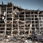 Abandoned multi-story building in desolate landscape with wrecked cars