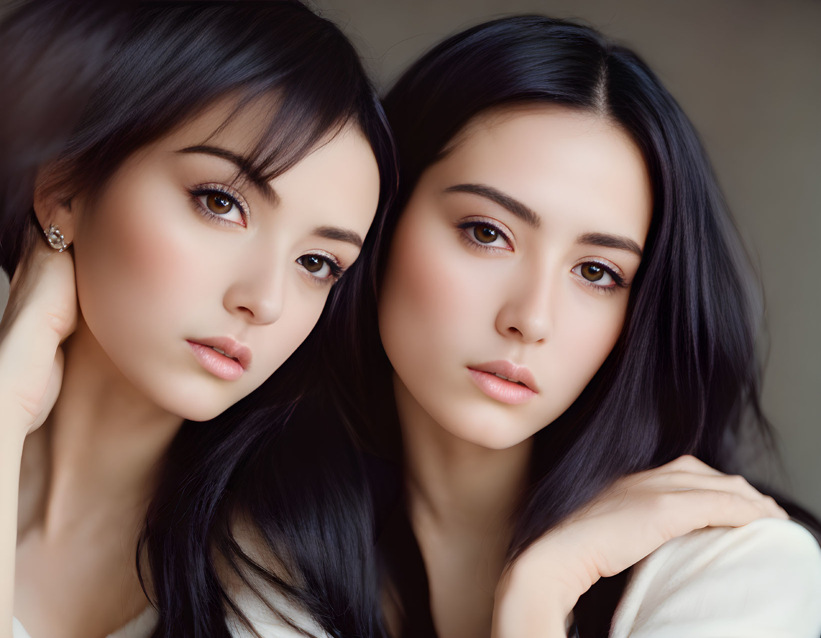 Two women with dark hair and fair skin in close pose, one touching cheek, other resting chin on