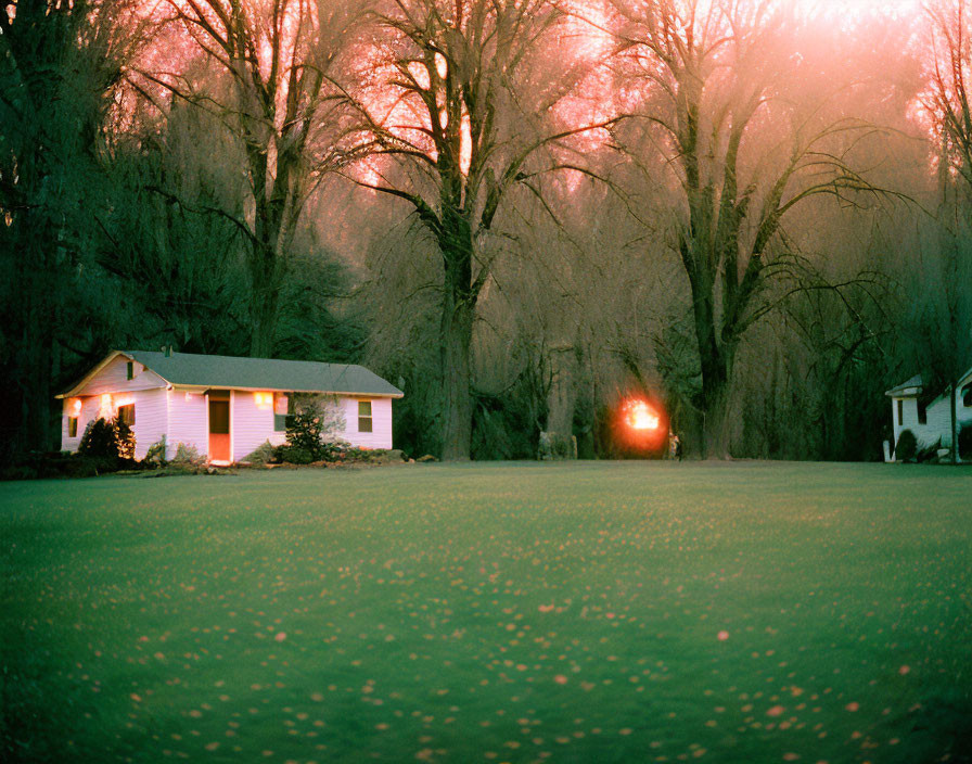 Twilight scene of white house with red lights, bare trees, and glowing sun.