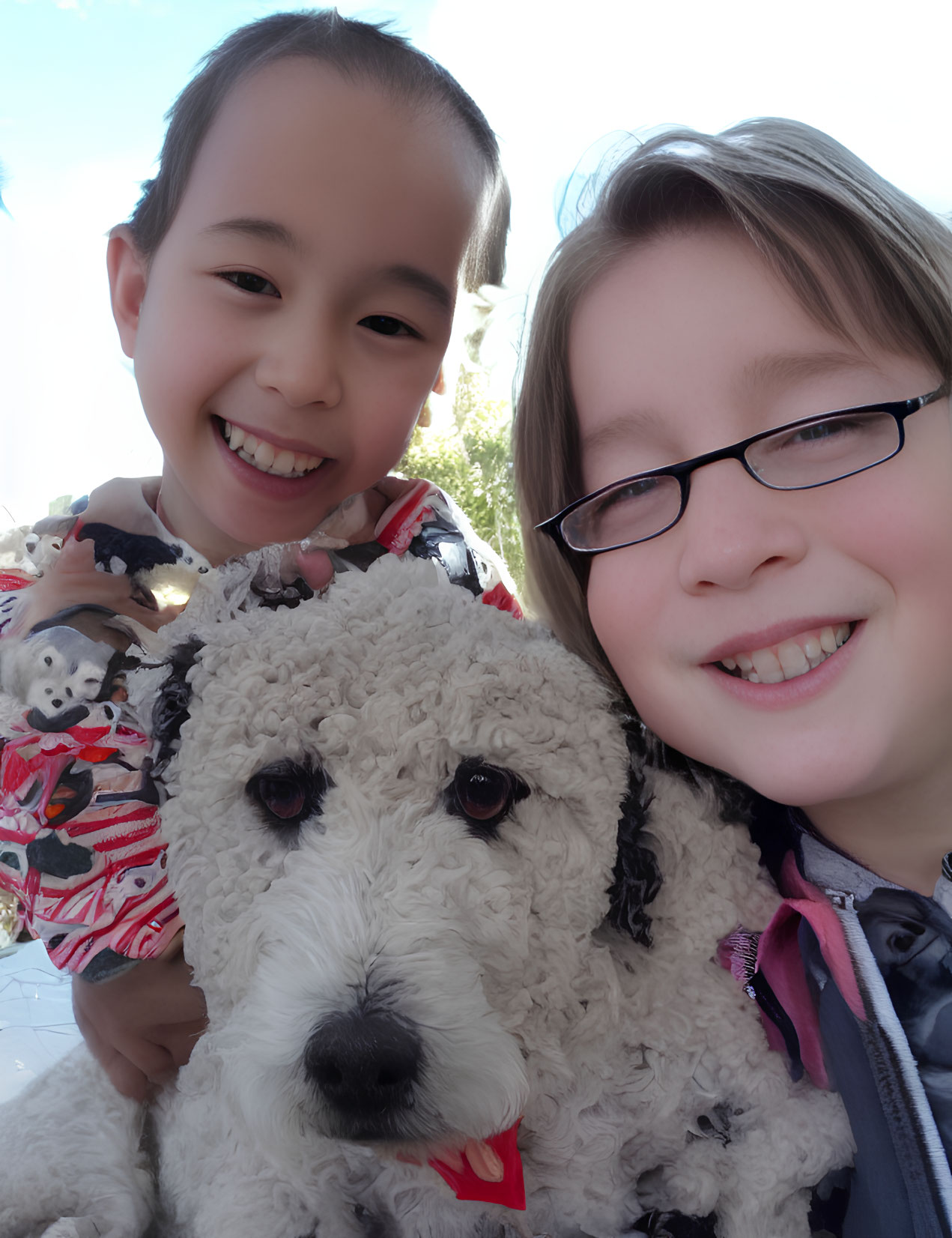 Smiling children with black and white dog in bright daylight