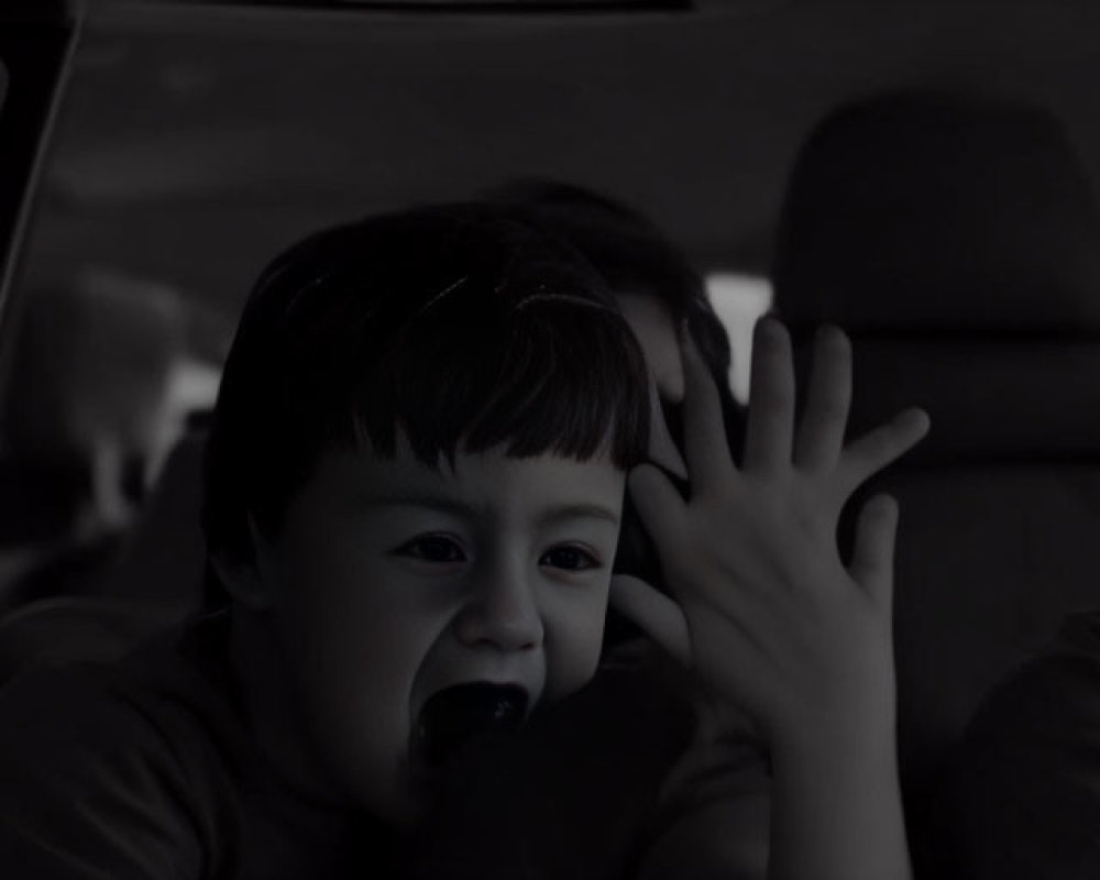 Distressed children in car: one crying, one yelling, monochrome.