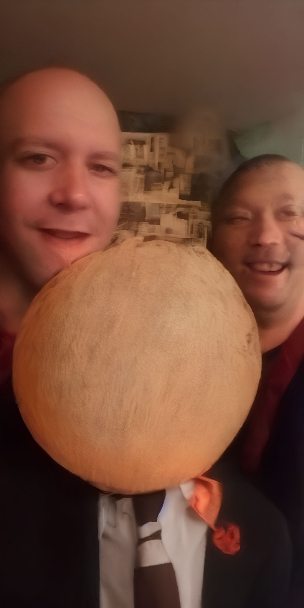 Men posing with large blurred fruit or vegetable.