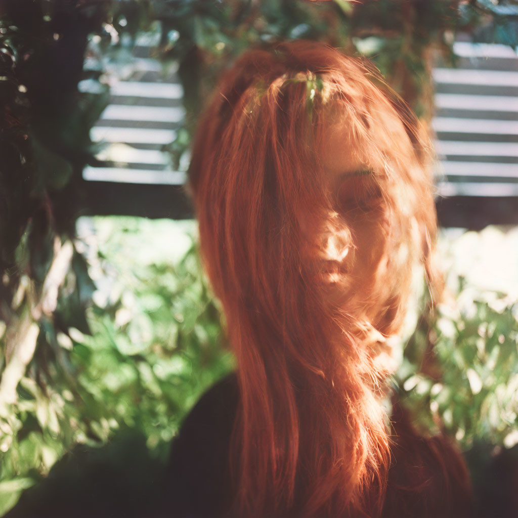 Red-haired woman obscured by hair in dappled sunlight.