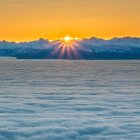 Sunrise over snowy landscape with textured clouds and warm orange hues.