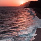 Surreal landscape with wavy sea patterns merging into mountain terrain at sunset