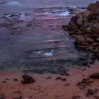 Colorful sunset over rocky shoreline with reflections in tide pools under purple sky