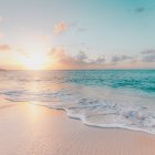 Tranquil beach sunrise with pastel sky, waves, hot air balloon, and birds