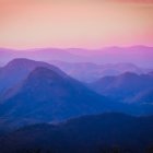 Tranquil landscape: Layered blue and pink mountain ranges under soft orange sky