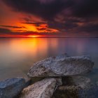 Vibrant sunset over calm lake with silhouetted mountains and colorful coral-like trees