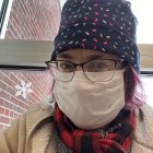 Portrait of person with white hair in cat-themed hat against ornate snowy building