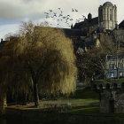 Castle on hill surrounded by autumn trees, calm water, dramatic sky