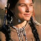 Woman adorned with intricate tribal jewelry: feather earrings, beaded neckpieces, decorative headpiece