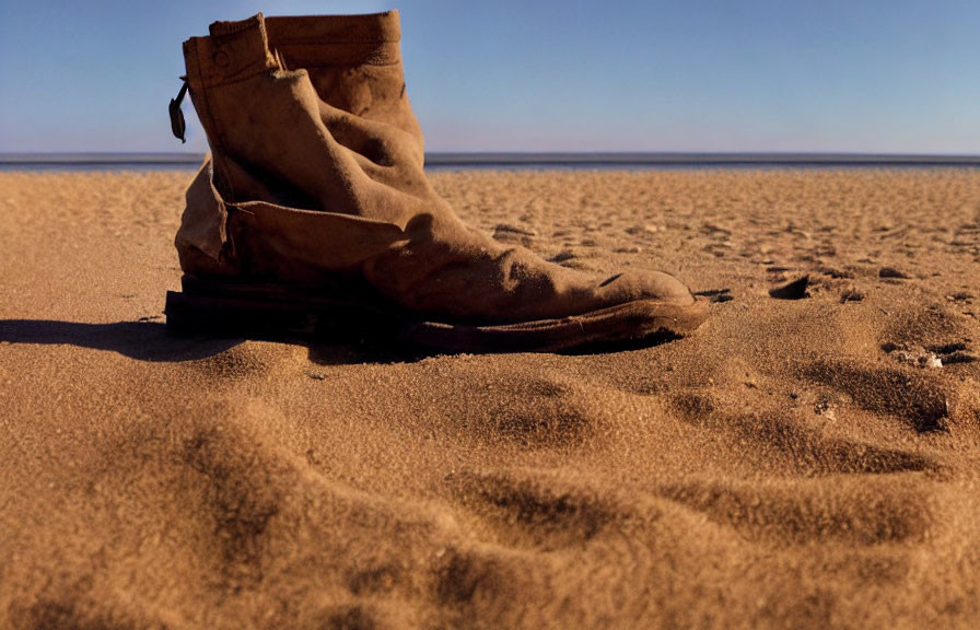 Abandoned worn-out boot in sandy desert under clear blue sky